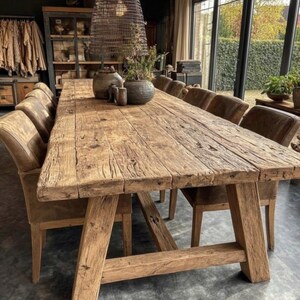 May include: A substantial, reclaimed wood dining table with a weathered appearance. The table, supported by angled legs, is surrounded by upholstered chairs. Decorative vases and plants are arranged on the table, creating a welcoming dining space.