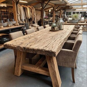 May include: A substantial, reclaimed wood dining table with a textured surface and angled supports. It is surrounded by upholstered chairs. The natural wood tones and texture create a warm, inviting atmosphere. The table is approximately 300 cm long.