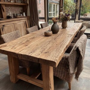 May include: A large, rustic wooden dining table with a natural, unfinished appearance. The table is supported by thick legs and surrounded by woven wicker chairs. Decorative vases and a small bowl sit on the table's surface. The table is approximately 254 cm long.