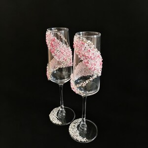 K&ouml;nnte beinhalten: Zwei Sektgl&auml;ser mit klarem Glas und einem dekorativen Design. Das Design zeigt rosa und silberne Verzierungen, die sich um das Glas winden. Der Fu&szlig; jedes Glases ist ebenfalls mit silbernen Verzierungen verziert.