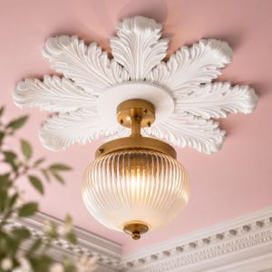 May include: A ceiling light fixture featuring a brass-toned metal mount and a round, ribbed clear glass shade. The fixture is centered on a large, white, circular ceiling medallion with intricate, carved leaf-like petal details.