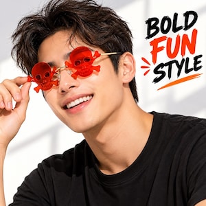 Puede incluir: Gafas de sol de novedad con lentes rojas translúcidas en forma de calavera, huesos cruzados integrados y monturas finas de metal dorado. El texto BOLD FUN STYLE está impreso en negro y naranja en el lado derecho de la imagen.