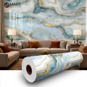 Op de afbeelding: Een rol behang met een marmerontwerp in tinten blauw, wit en goud. Het behang wordt gepresenteerd voor een muur met een vergelijkbaar ontwerp, met een woonkamersetting. De merknaam "MART COMFORT" is zichtbaar.