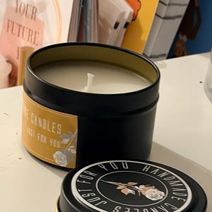 K&ouml;nnte beinhalten: Eine schwarze Kerzendose mit goldenem Rand, gef&uuml;llt mit wei&szlig;em Wachs und einem mittigen Docht. Das Etikett lautet "Rose Candles Just For You" mit einer Rosengrafik. Der Deckel tr&auml;gt den Text "Handmade Candles Just For You" um eine Rose.