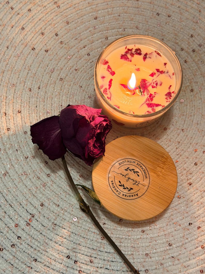 K&ouml;nnte beinhalten: Eine brennende Kerze in einem durchsichtigen Glas mit getrockneten Rosenbl&auml;ttern. Ein Holzdeckel mit dem Text "Thank you" und "Aveerah Candles" befindet sich neben der Kerze. Eine getrocknete burgunderfarbene Rose ist ebenfalls im Bild.