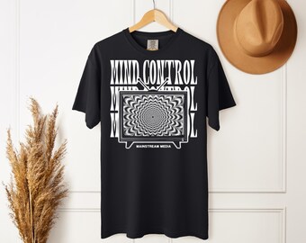 May include: A black short-sleeve t-shirt featuring a white graphic of a vintage television set displaying a hypnotic spiral pattern. The text MIND CONTROL is printed in large white letters above the television, with MAINSTREAM MEDIA below.