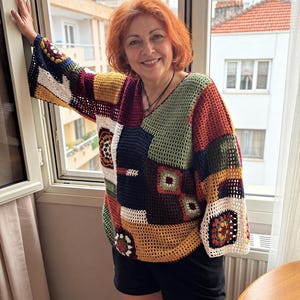 May include: A long-sleeved crochet jumper featuring a patchwork design of various square patterns in colours including mustard yellow, olive green, navy blue, white, and rust orange, paired with solid black shorts.