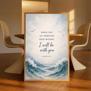 May include: A framed art print with a watercolor illustration of ocean waves and seagulls. The text reads "WHEN YOU GO THROUGH DEEP WATERS, I will be with you. ISAIAH 43:2." The frame is a light brown color.
