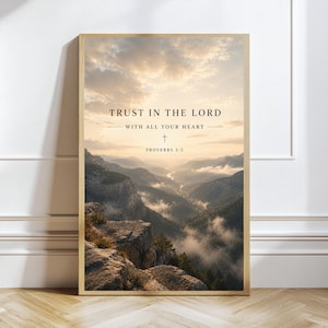 May include: A framed print featuring a scenic mountain landscape under a cloudy sky. The text "TRUST IN THE LORD WITH ALL YOUR HEART" is displayed at the top, with "PROVERBS 3:5" below. The frame is a light brown color.