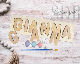 May include: Wooden puzzle with the name "GIANNA" cut out in individual letters. The letters are loose and can be placed in the cutouts. The puzzle comes with three small paint pots and a paintbrush.