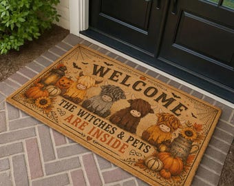 Puede incluir: Un felpudo rectangular de color tostado con ilustraciones de tres vacas Highland, calabazas, girasoles y telarañas. El texto WELCOME THE WITCHES & PETS ARE INSIDE aparece en letras negras y naranjas. La alfombra está sobre un suelo de ladrillo gris.