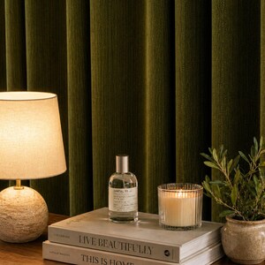 Peut inclure: Une lampe de table avec un abat-jour beige et une base sph&eacute;rique textur&eacute;e est pos&eacute;e &agrave; c&ocirc;t&eacute; d'un flacon de parfum, d'une bougie allum&eacute;e et d'une petite plante en pot. Les objets sont sur des livres avec les titres "LIVE BEAUTIFULLY" et "THIS IS HOME".