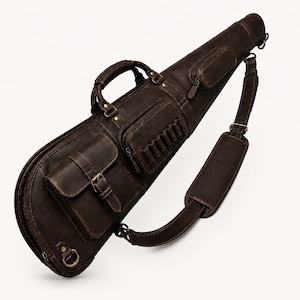 May include: A dark brown leather gun case featuring a top handle, an adjustable shoulder strap with a padded section, and multiple exterior storage pockets. One pocket includes a flap with a buckle closure, while another features a row of loops.