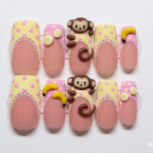 May include: A set of ten artificial nails with a playful design. The nails feature a light pink base with yellow polka dots, a scalloped edge, and a monkey or banana embellishment. The nails are designed for a fun and unique look.