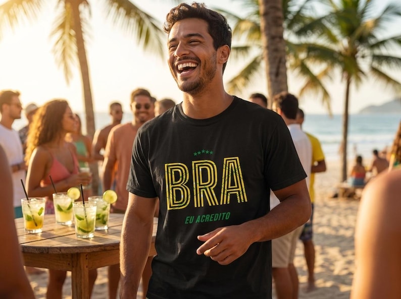 May include: A black t-shirt with the word "BRA" in yellow and green, with the phrase "EU ACREDITO" below. The shirt is worn by a smiling person on a beach, with a group of people and cocktails in the background.