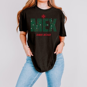May include: Black t-shirt with the word "MEX" in green, with a red diamond design above the text. Below the text is the phrase "VAMOS M&Eacute;XICO" in red. The shirt is worn with blue jeans.