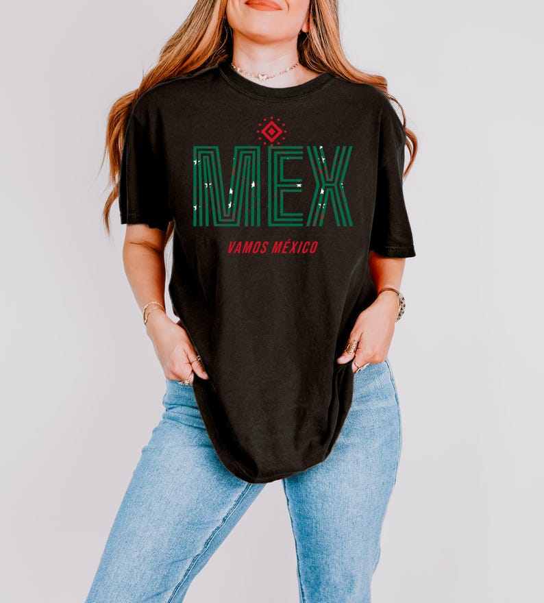 May include: Black t-shirt with the word "MEX" in green, with a red diamond design above the text. Below the text is the phrase "VAMOS M&Eacute;XICO" in red. The shirt is worn with blue jeans.