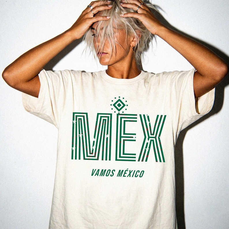 May include: Cream-colored t-shirt with the word "MEX" in green, stylized with vertical stripes and stars. Below, the text reads "VAMOS M&Eacute;XICO". The shirt has a crew neck and short sleeves.