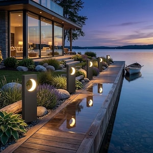 May include: A series of rectangular dark gray outdoor bollard lights with illuminated crescent moon cutouts lining a wooden dock at dusk. The lights cast a warm glow onto the wet planks, reflecting the moon shapes alongside a small boat on the water.