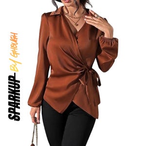 Puede incluir: Una blusa cruzada de satén color óxido de manga larga con cuello, puños fruncidos y cierre de lazo lateral. El texto "SPARKUP BY GHOUGH" está impreso verticalmente en naranja y negro en el lado izquierdo de la imagen.