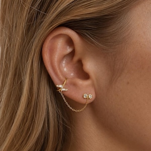 Peut inclure: Manchette d'oreille et boucles d'oreilles doubles dorées. La manchette d'oreille présente un motif de libellule avec des cristaux transparents. Une chaîne délicate relie la manchette aux boucles d'oreilles doubles, chacune avec un cristal clair.