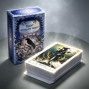 Może przedstawiać: Zestaw kart tarota i pudełko. Pudełko jest niebieskie z napisem "SILENT DESOLATE TAROT" i ilustracją kruka. Karty są ułożone w stos, a górna karta przedstawia postać w lesie. Karta głosi "0. THE FOOL."