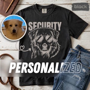 May include: A black short-sleeved t-shirt featuring a graphic of a dog wearing aviator sunglasses with the word SECURITY printed above. A circular inset shows a photograph of a light-colored dog, connected by a heart-shaped arrow graphic.