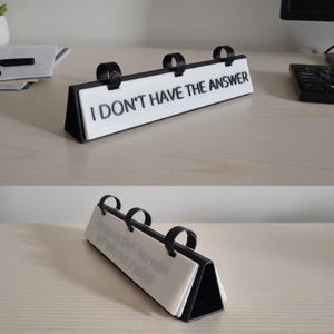 May include: A black triangular desk sign with three black rings holding white rectangular panels. The front panel features the black text I DON'T HAVE THE ANSWER. The structure is designed to flip through multiple panels for display on a flat surface.