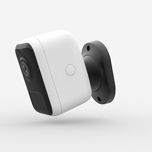 May include: A white and black security camera with a rounded rectangular shape. The camera has a black lens and a black mounting bracket. A small, circular button is on the front of the camera.