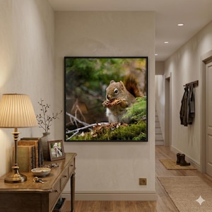 May include: A framed print of a squirrel eating a nut, set against a backdrop of green foliage. The squirrel is brown with a bushy tail. The artwork hangs on a neutral-colored wall in a hallway, with a wooden table and lamp in the foreground.
