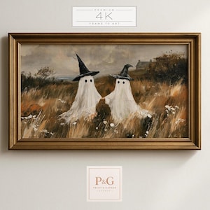 May include: A rectangular wall art piece in a gold frame featuring an oil painting of two white ghosts wearing black witch hats standing in a field of tall brown grass under a cloudy sky. The text PREMIUM 4K FRAME TV ART is visible above.