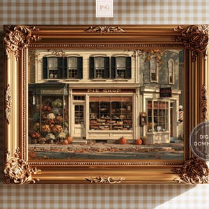 Puede incluir: Una impresión artística enmarcada que representa una escena callejera con una floristería y una pastelería. Los escaparates cuentan con grandes ventanales, contraventanas oscuras y decoraciones otoñales que incluyen calabazas en la acera. El marco dorado ornamentado rodea la ilustración detallada de los edificios y la calle cubierta de hojas caídas.