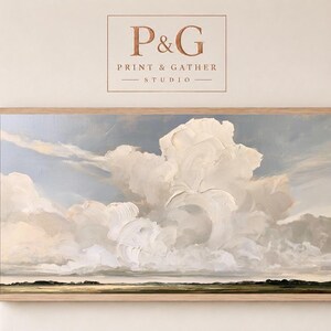 Puede incluir: Un cuadro de paisaje horizontal en un marco de madera clara con grandes nubes texturizadas blancas y crema sobre un cielo azul suave, encima de una línea de horizonte oscura y baja. Arriba de la obra aparece el texto P&G PRINT & GATHER STUDIO.