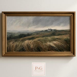 May include: A landscape painting in a rectangular gold frame depicting a grassy field under a dark, stormy sky. The scene features rolling hills, tall wind-swept grasses in the foreground, and a small white house situated in the distance.