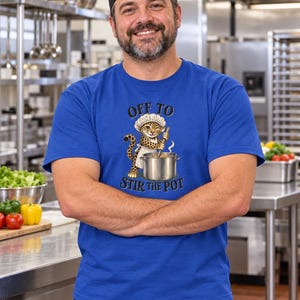 May include: A royal blue short-sleeved t-shirt featuring a graphic of a leopard wearing a chef hat and apron, stirring a large metal pot. The text above the leopard reads OFF TO and the text below the leopard reads STIR THE POT in black.