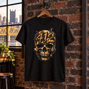 May include: A black short-sleeve t-shirt featuring a graphic print of a human skull in shades of gold and yellow. The number 412 is prominently displayed across the forehead of the skull in a bold, distressed font style with smoke-like effects.