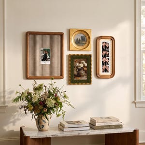 May include: A gallery wall arrangement featuring a large rectangular wooden frame with a striped fabric backing, a small circular gold frame, a rectangular green velvet frame with gold beads, and a tall wooden frame containing a photo strip.