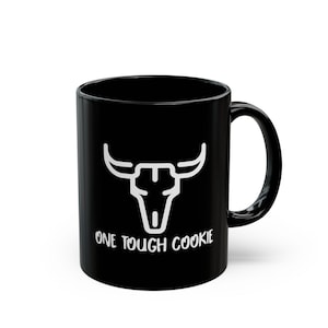 May include: Black ceramic mug with a white bull skull graphic and the text "ONE TOUGH COOKIE". The mug has a curved handle and a glossy finish. A great gift for coffee or tea lovers.