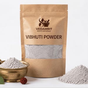 May include: A brown paper pouch labelled VEDAMRIT ROOTS NATURALS VIBHUTI POWDER containing fine grey powder. Beside it sits a brass bowl filled with the same grey powder, a small spoon, three green leaves, a brown seed, and a pile of grey powder.