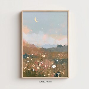 Pode incluir: Uma impressão de arte emoldurada com uma pintura de paisagem serena. A obra de arte retrata um campo de flores silvestres sob um céu pastel com uma lua crescente. A paleta de cores inclui azuis, rosas e castanhos suaves, criando uma estética calma. O texto "SONORA PRINTS" está na parte inferior.