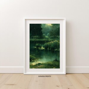 Pode incluir: Uma impressão de arte emoldurada retrata uma paisagem serena com um lago escuro e reflexivo, cercado por vegetação exuberante e árvores. A obra de arte está em uma moldura branca e está rotulada como "SONORA PRINTS" na parte inferior.