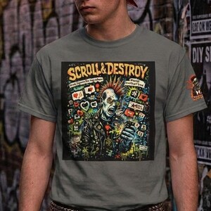 May include: A grey short-sleeved t-shirt featuring a graphic print of a punk character with a red mohawk looking at a smartphone. The text reads SCROLL & DESTROY. The shirt has a small logo on the sleeve and is paired with black jeans.