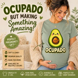 May include: A sage green t-shirt featuring a cartoon avocado with a smaller avocado inside, accompanied by the text "OCUPADO" and "BUT MAKING SOMETHING AMAZING!". The design includes a circular badge with the text "PERFECT PREGNANCY GIFT!" and a list of features including "SOFT & COMFY", "PREMIUM QUALITY", "MADE FOR MOMS", and "AVAILABLE IN MULTIPLE COLORS".