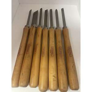 May include: A set of seven woodturning chisels with light-coloured wooden handles and metal blades. Each handle is stamped with the brand name GENERAL in a rectangular border. The tools feature various blade shapes including gouges and skews.