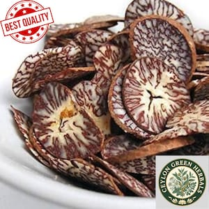 Pode incluir: Close-up de nozes de betel secas e fatiadas, exibindo um padrão distinto de marmoreio marrom e branco. As nozes estão dispostas em uma tigela branca, com um selo "Best Quality" no canto superior esquerdo e um logotipo "Ceylon Green Herbals" no canto inferior direito.