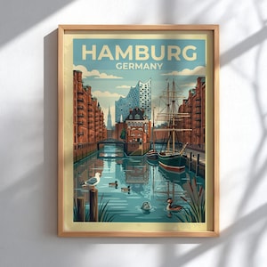 Könnte beinhalten: Ein gerahmtes Reiseplakat mit dem Text HAMBURG GERMANY. Die Illustration zeigt eine Kanalszene mit roten Backsteingebäuden, einem großen Segelschiff, der Elbphilharmonie, einer Möwe auf einem Pfahl, Enten und einer Robbe im Wasser.