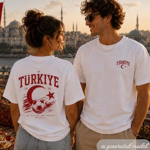 May include: A white short-sleeve t-shirt featuring a red graphic on the back with the text T&Uuml;RKIYE, a crescent moon, a star, a soccer ball, and the text ONE NATION ONE DREAM 2026. The front chest displays the text T&Uuml;RKIYE with a small crescent and star.