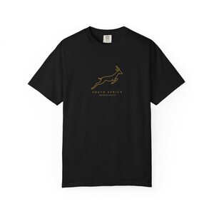 A black t-shirt with a gold outline of a jumping springbok and the words "SOUTH AFRICA AMABOKOBOKO" below it, laid flat on a white background.
