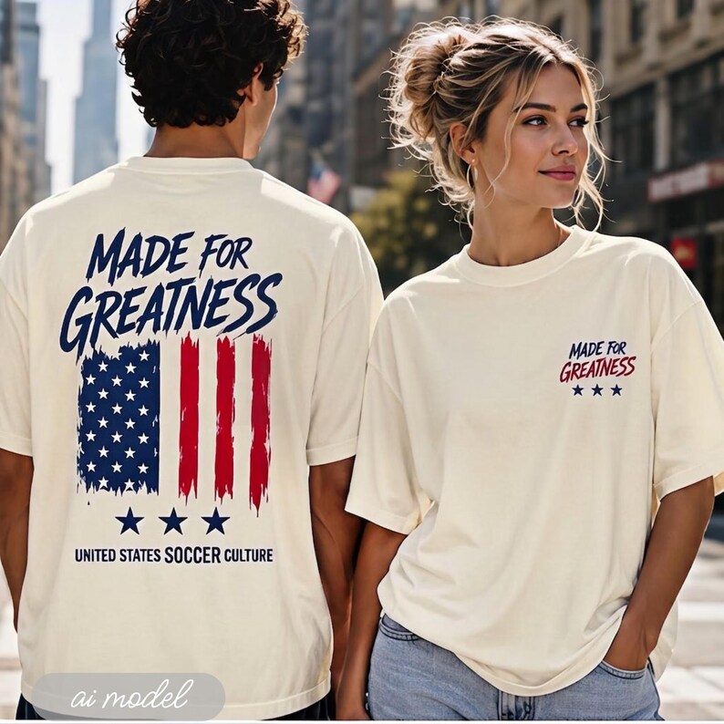 以下が含まれることがあります： オフホワイトのTシャツ。背面には「MADE FOR GREATNESS」の文字とデフォルメされたアメリカ国旗、「UNITED STATES SOCCER CULTURE」の文字がプリントされ、胸元には小さな「MADE FOR GREATNESS」のロゴが入っています。
