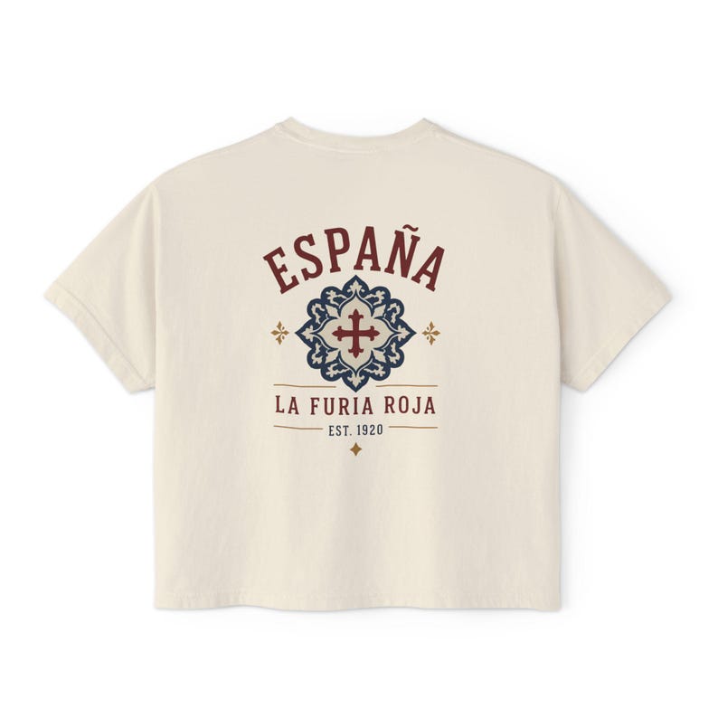 The back of a cream-colored short-sleeved crop top, showing "ESPAÑA LA FURIA ROJA EST. 1920" in red and blue with a tile graphic, shown flat against a white background.
